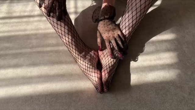 Girl in fishnet tights gently caresses her legs while stroking them in lace gloves